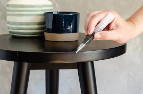 Hand with silver-tipped paint pen kit poised over black stool
