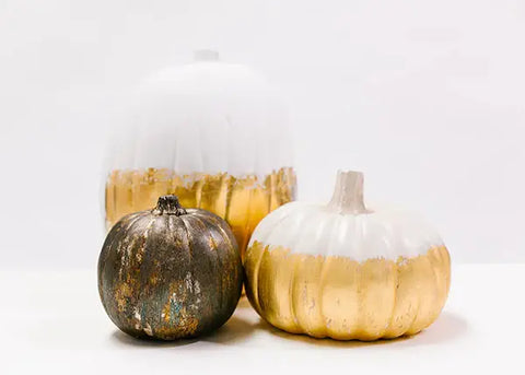 Two decorative gold leaf pumpkins, one metallic distressed, one gold and white